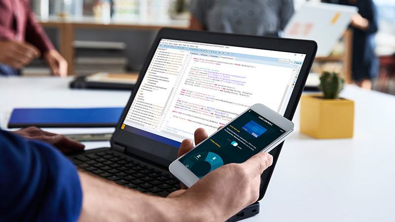 Developer in office environment with open laptop looking at smart phone.