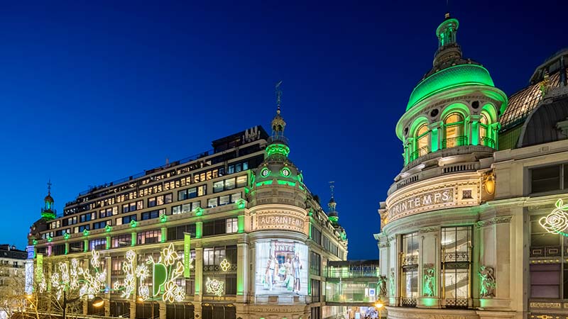 Illuminated historic building at night with green domes and ornate architecture, adorned with glowing floral patterns.