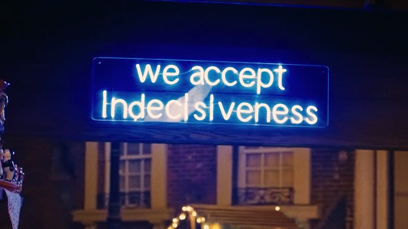 Blue neon sign reads "we accept indecisiveness," glowing warmly against a dark backdrop. The setting exudes a quirky, welcoming vibe.